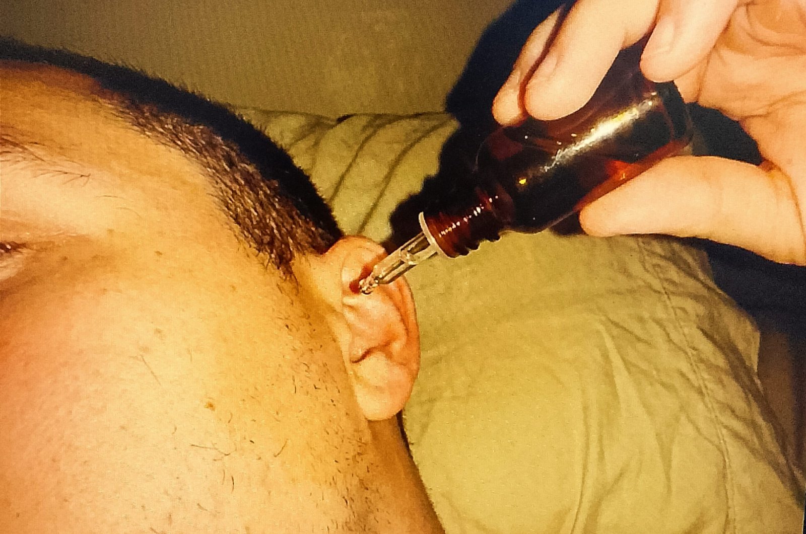 IMG ٢٠٢٥١٢١١ ١٥٢٤١٩ scaled Close-up of a hand holding a dropper bottle containing clear oil, positioned over a specifically tilted ear (model lying on their side).