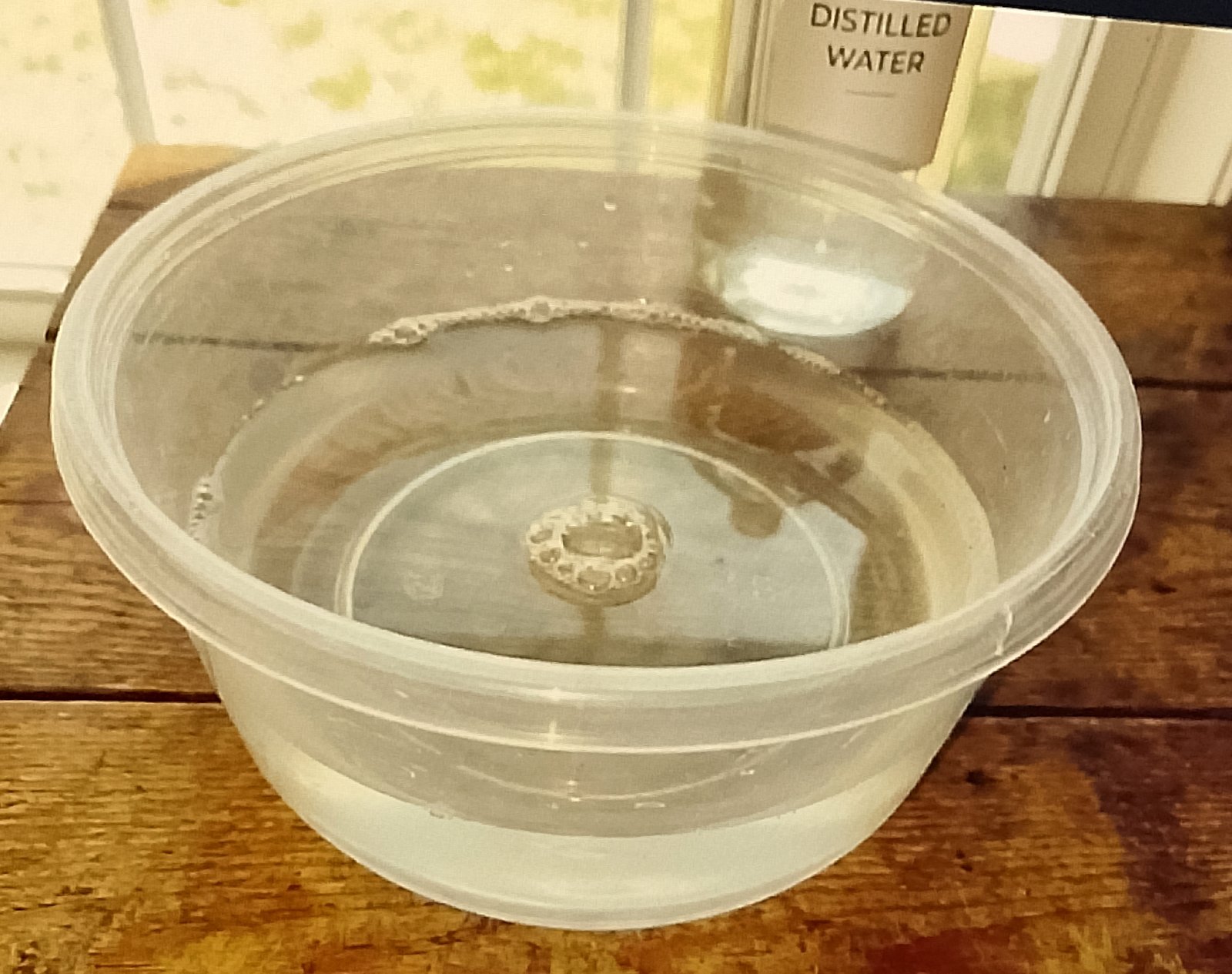 Close-up of the plastic container with warm water and bubbles, with the bottle of distilled water visible in the background