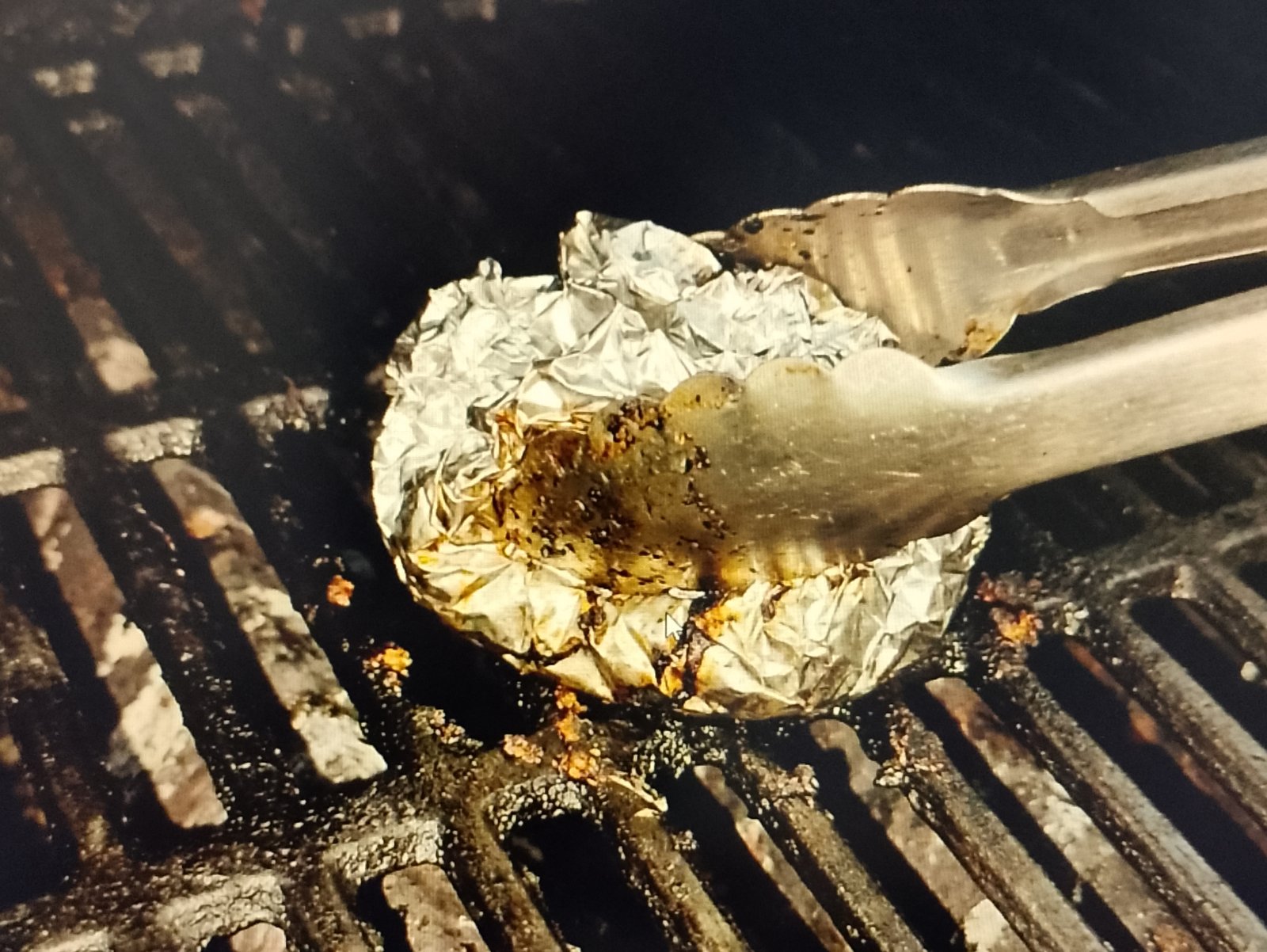 Cleaning grill grates with aluminum foil held by tongs