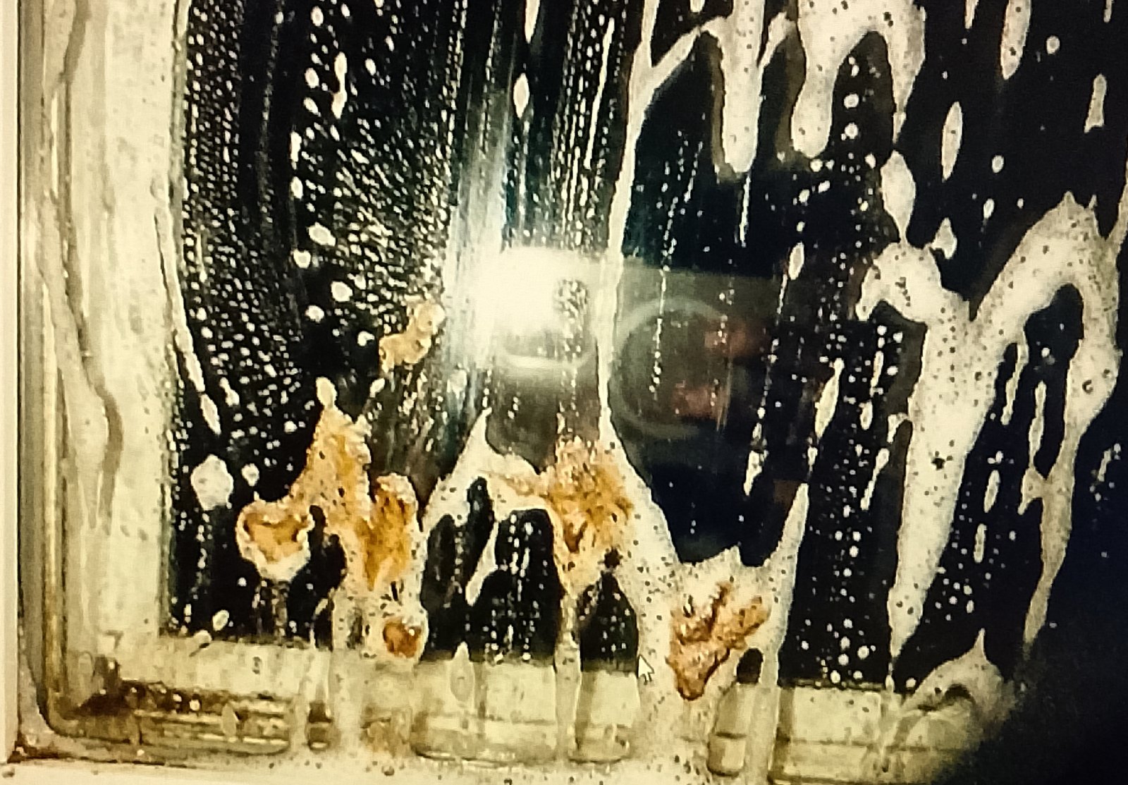 Action shot of the window covered in wet suds, focusing on a corner where the dirt is visibly lifting.
