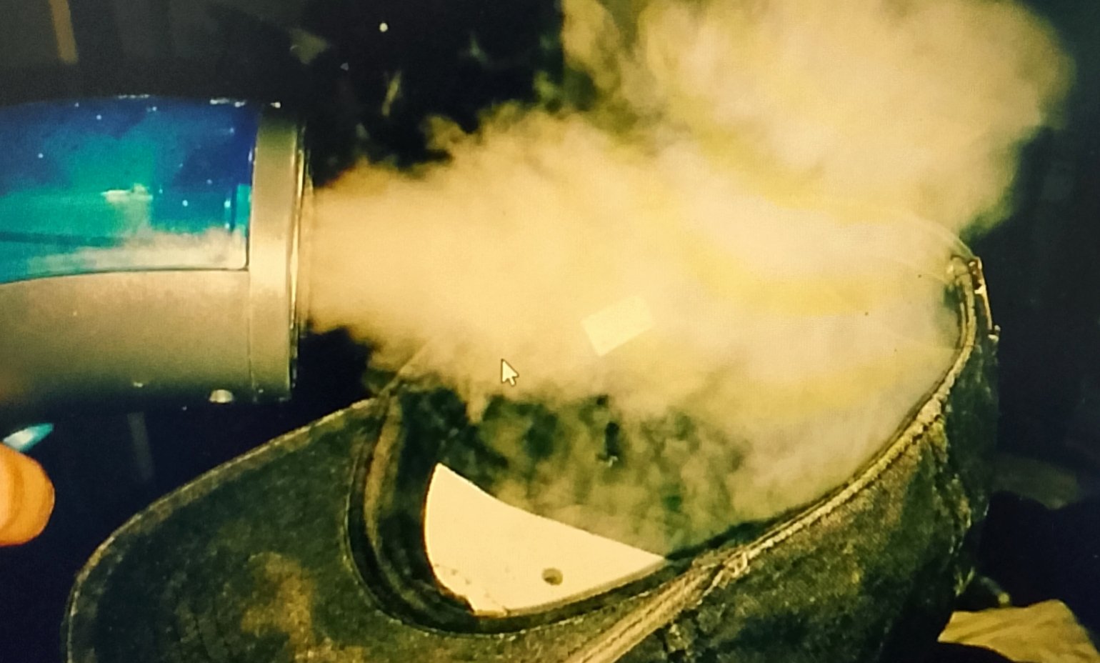 baseball cap A handheld steamer releasing a cloud of vapor into the interior of a baseball cap