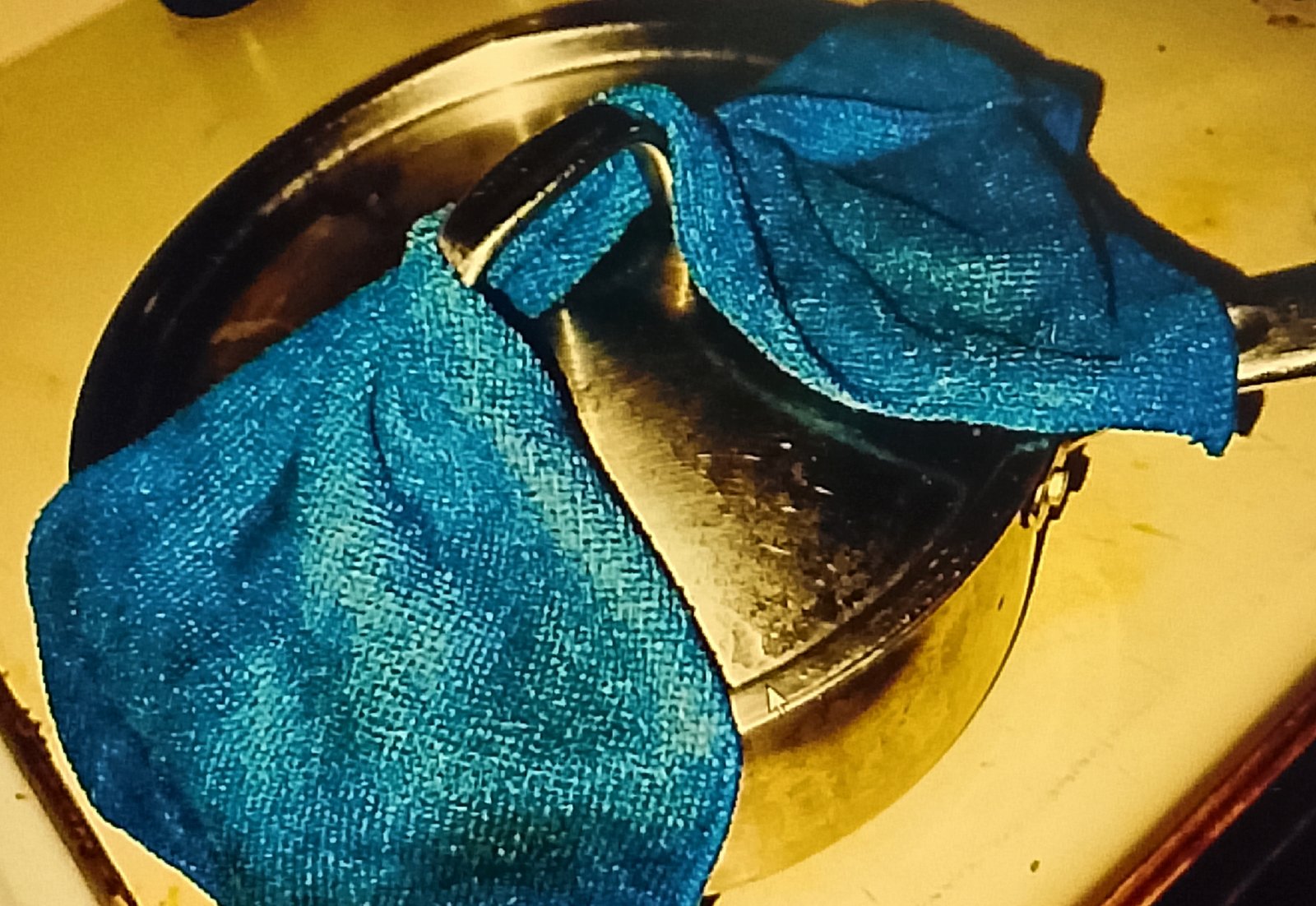 Microfiber cloth wrapped tightly around a metal pot lid for cleaning
